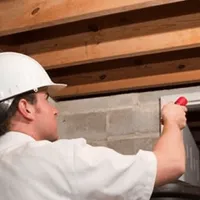 Termite inspection technician checking a basement wall and framing for termite activity in West Palm Beach, FL